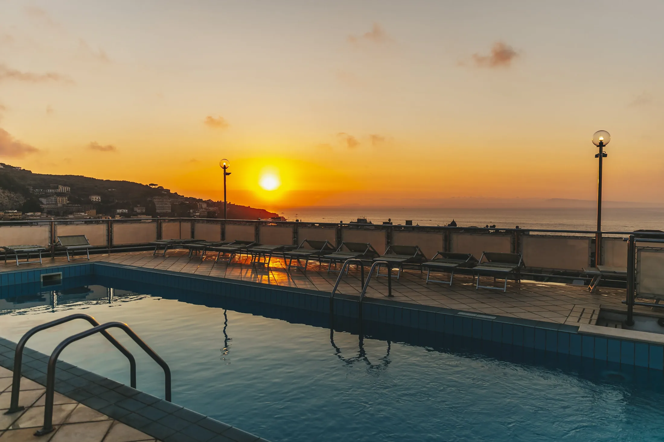 Piscina all’aperto al tramonto con vista sul mare e lettini sul terrazzo