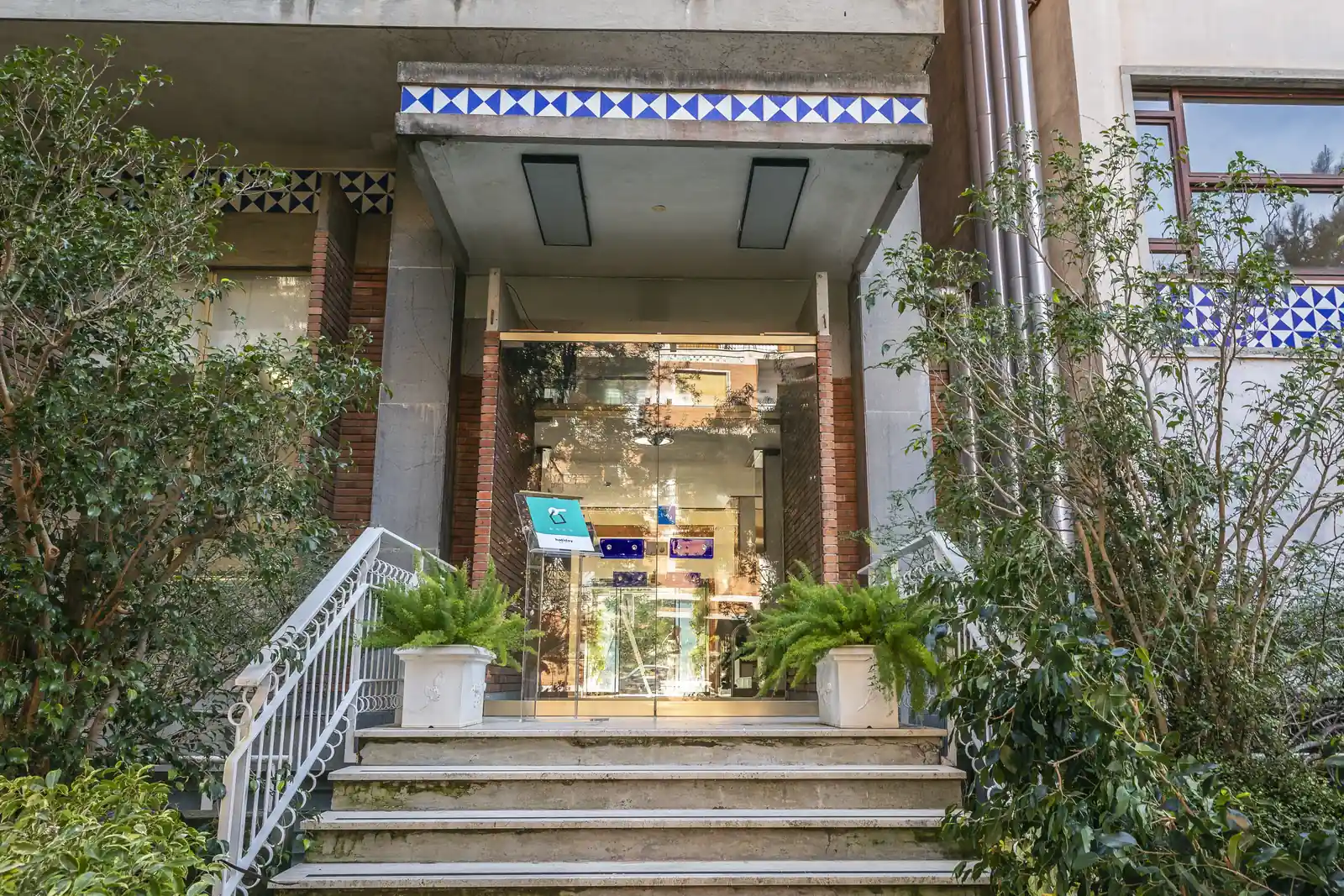 Ingresso di un edificio con scale, vetrata e piante ornamentali ai lati