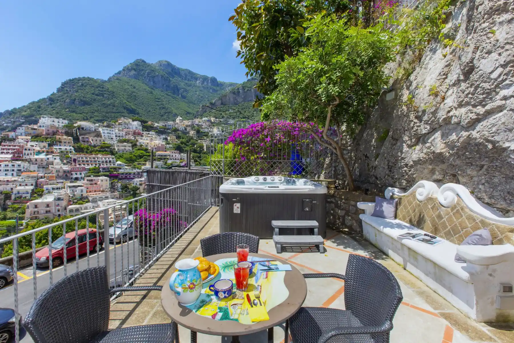 Terrazza panoramica con tavolo apparecchiato, vasca idromassaggio e vista sul borgo costiero e sulle montagne