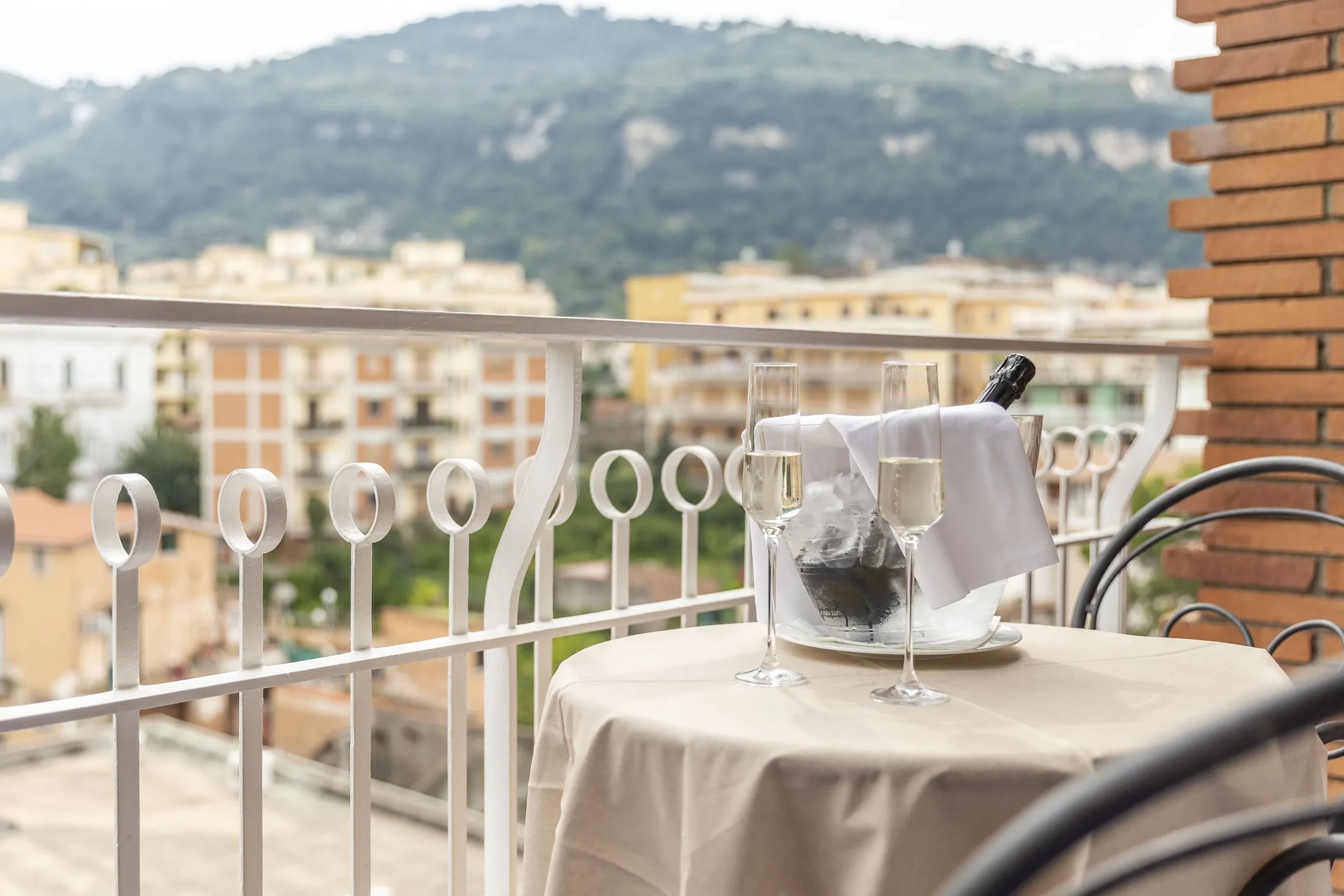 Tavolo apparecchiato su un balcone con champagne, bicchieri e vista sulle montagne e sulla città