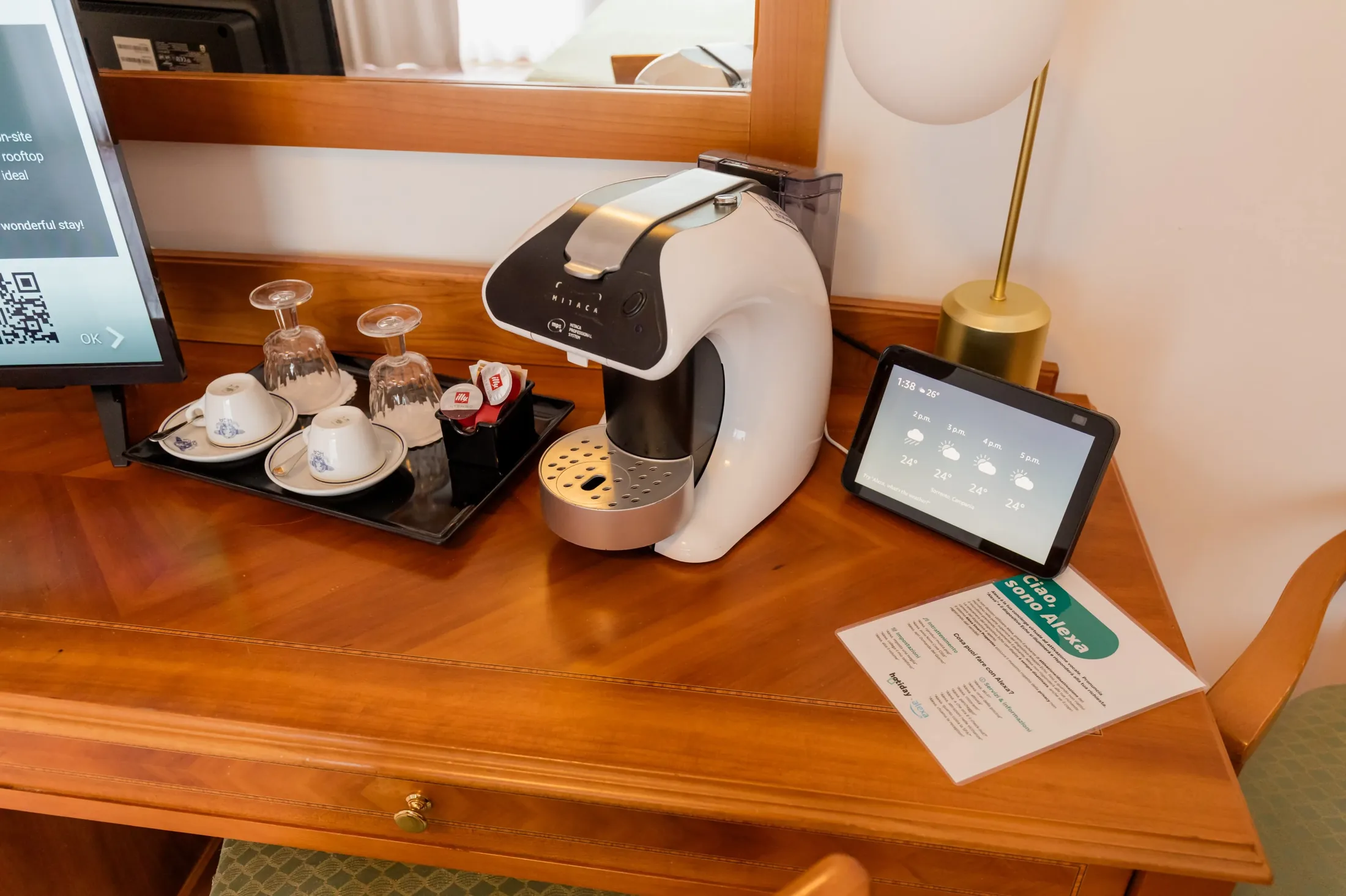 Macchina da caffè con tazze, bicchieri e tablet informativo su un tavolo in camera d’albergo