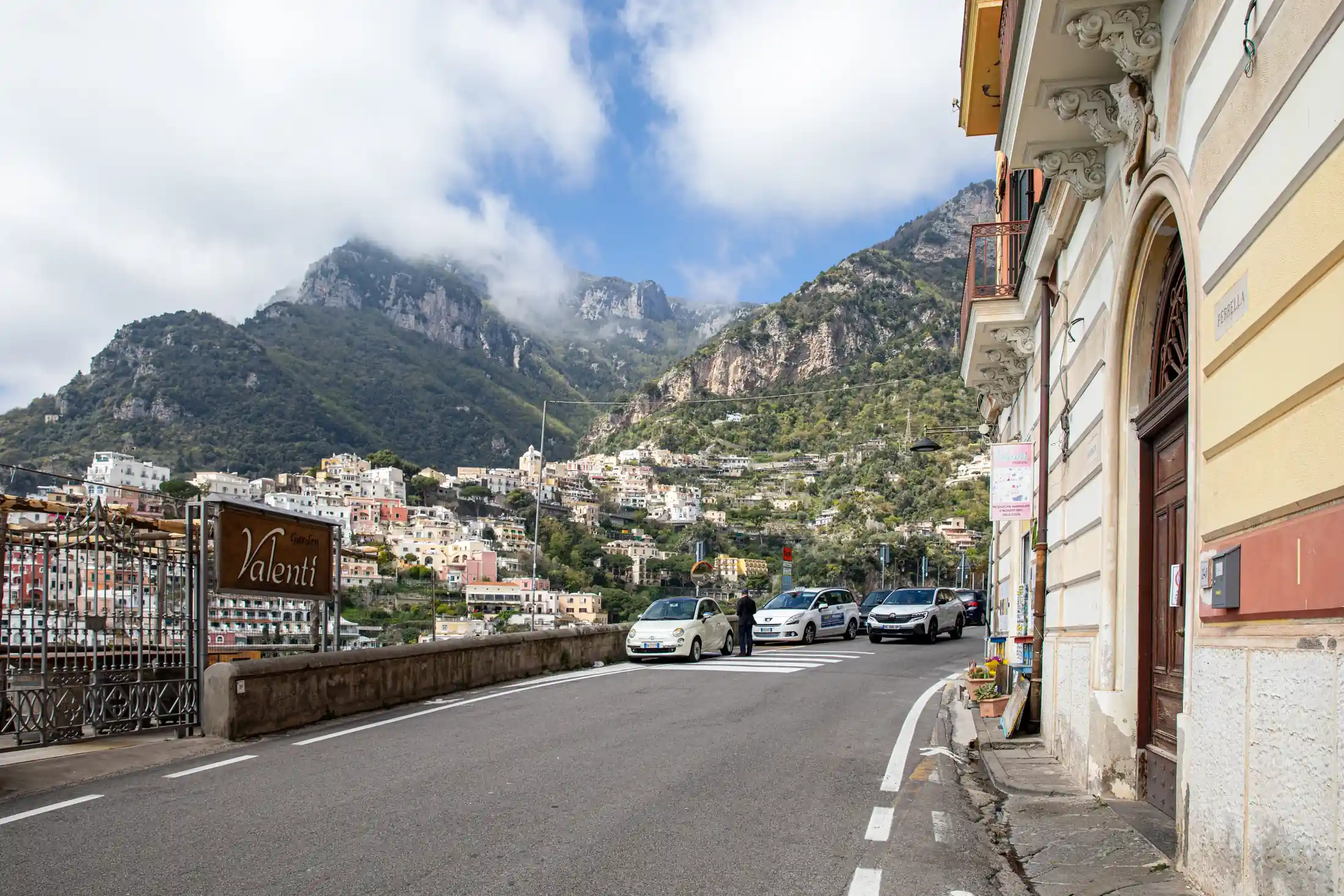 Strada panoramica a Positano con auto parcheggiate e montagne sullo sfondo
