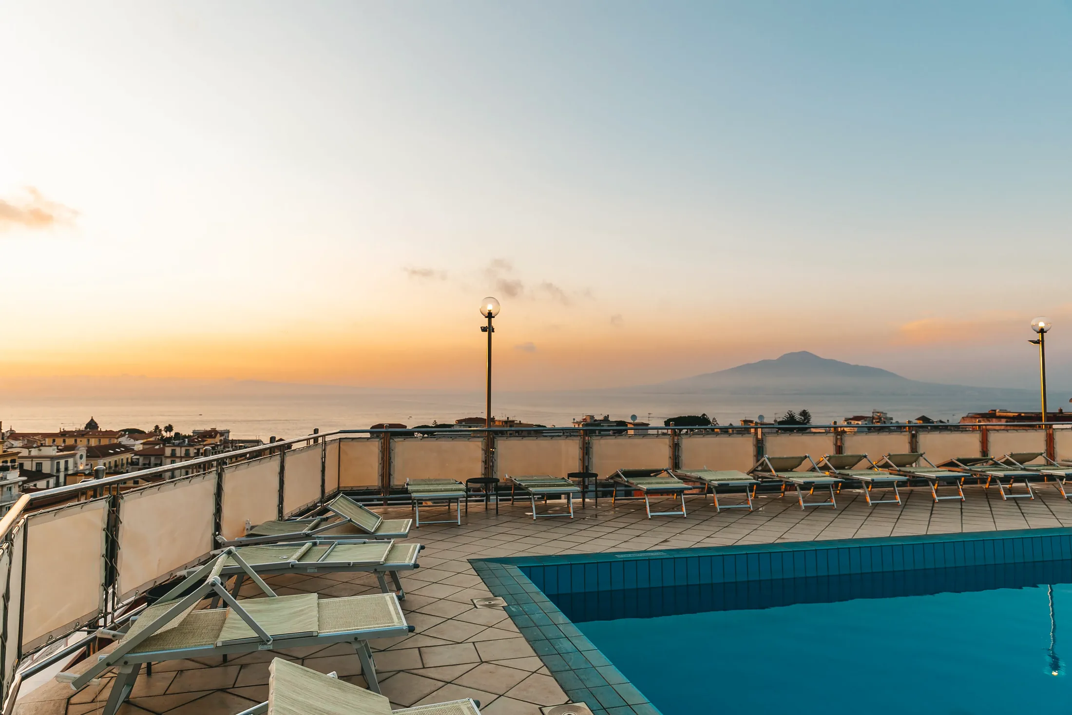 Piscina panoramica sul tetto con lettini, vista sul mare e sul Vesuvio all’alba